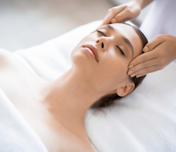 Young relaxed woman enjoying facial massage in professional spa salon