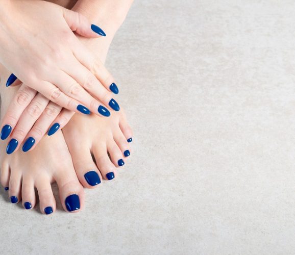 Young lady is showing her blue manicure and pedicure nails, grey background, copy space